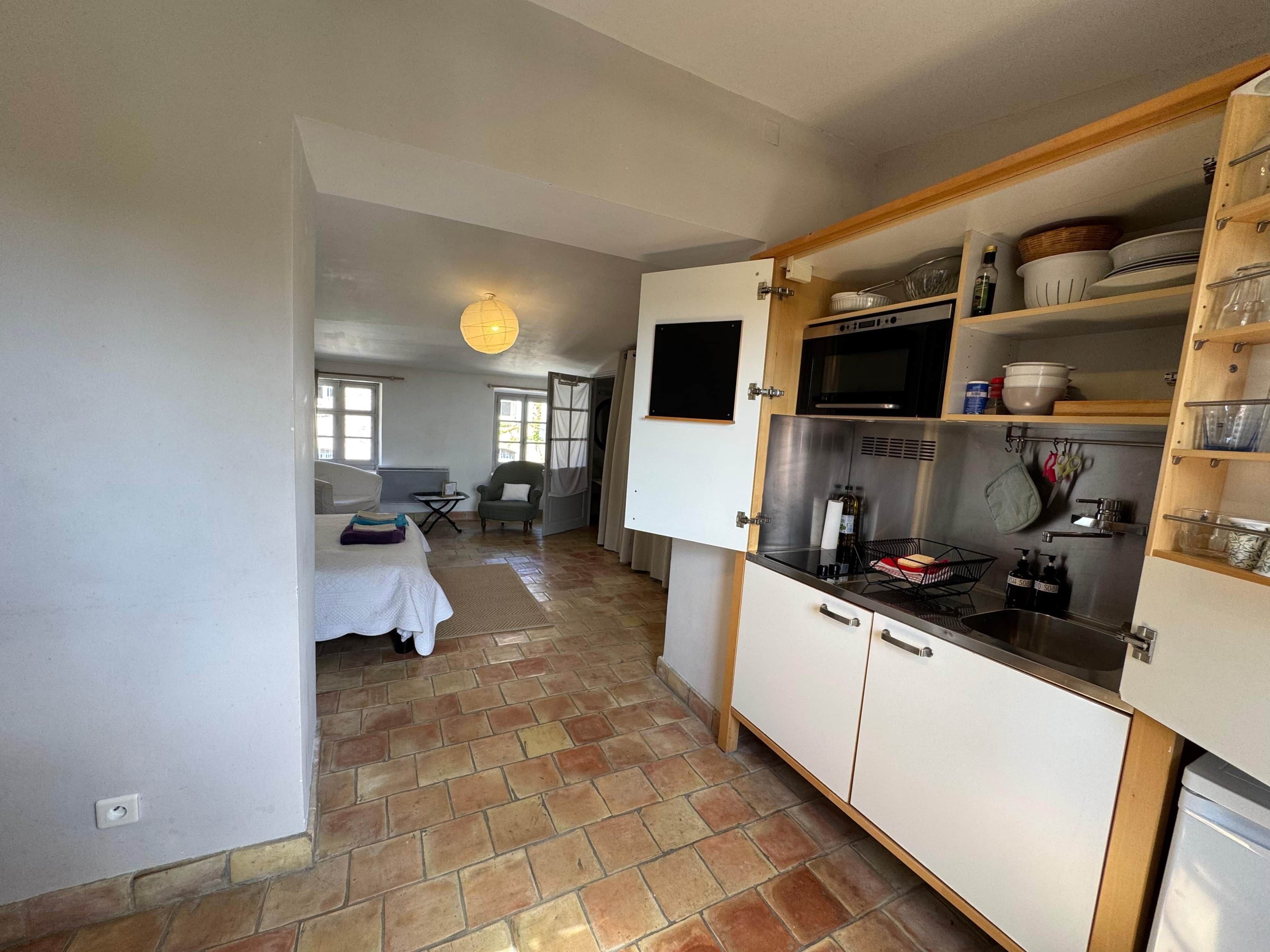 Una cocina compacta con microondas, estufa y diversos utensilios de cocina. Se ve un área de comedor con una mesa y sillas al fondo.