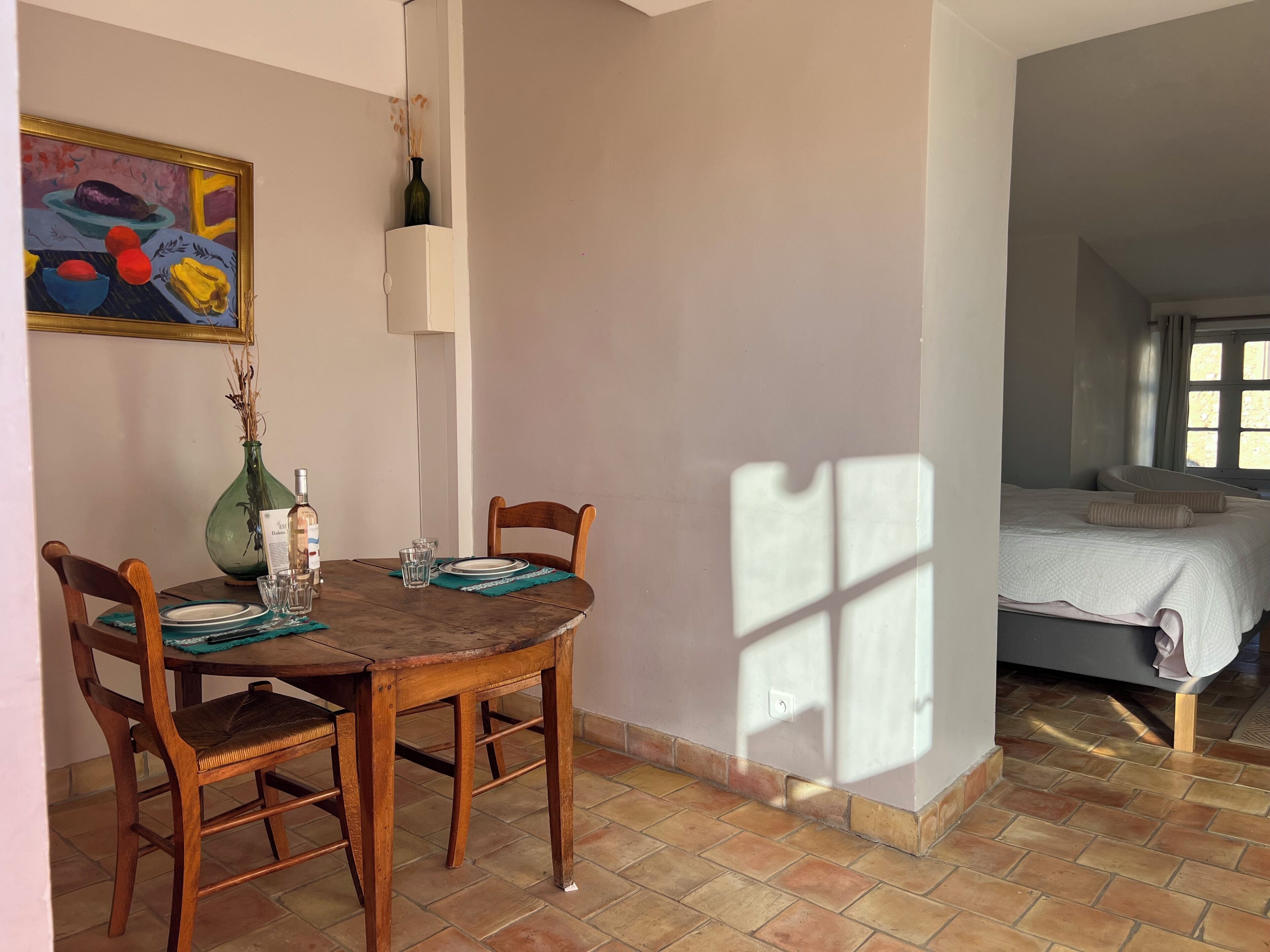 Un coin repas avec une table en bois, des chaises, un vase contenant des plantes séchées et un tableau accroché au mur.