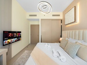A hotel room with a bed, a flat-screen TV mounted on the wall, a bedside table, and a headboard.