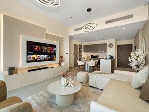 A modern living room with a flat-screen TV, a round coffee table, and a sofa. There is a kitchen area visible in the background.