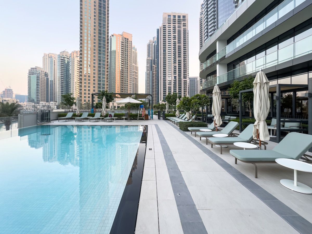 A rooftop swimming pool with lounge chairs and umbrellas, surrounded by high-rise buildings.