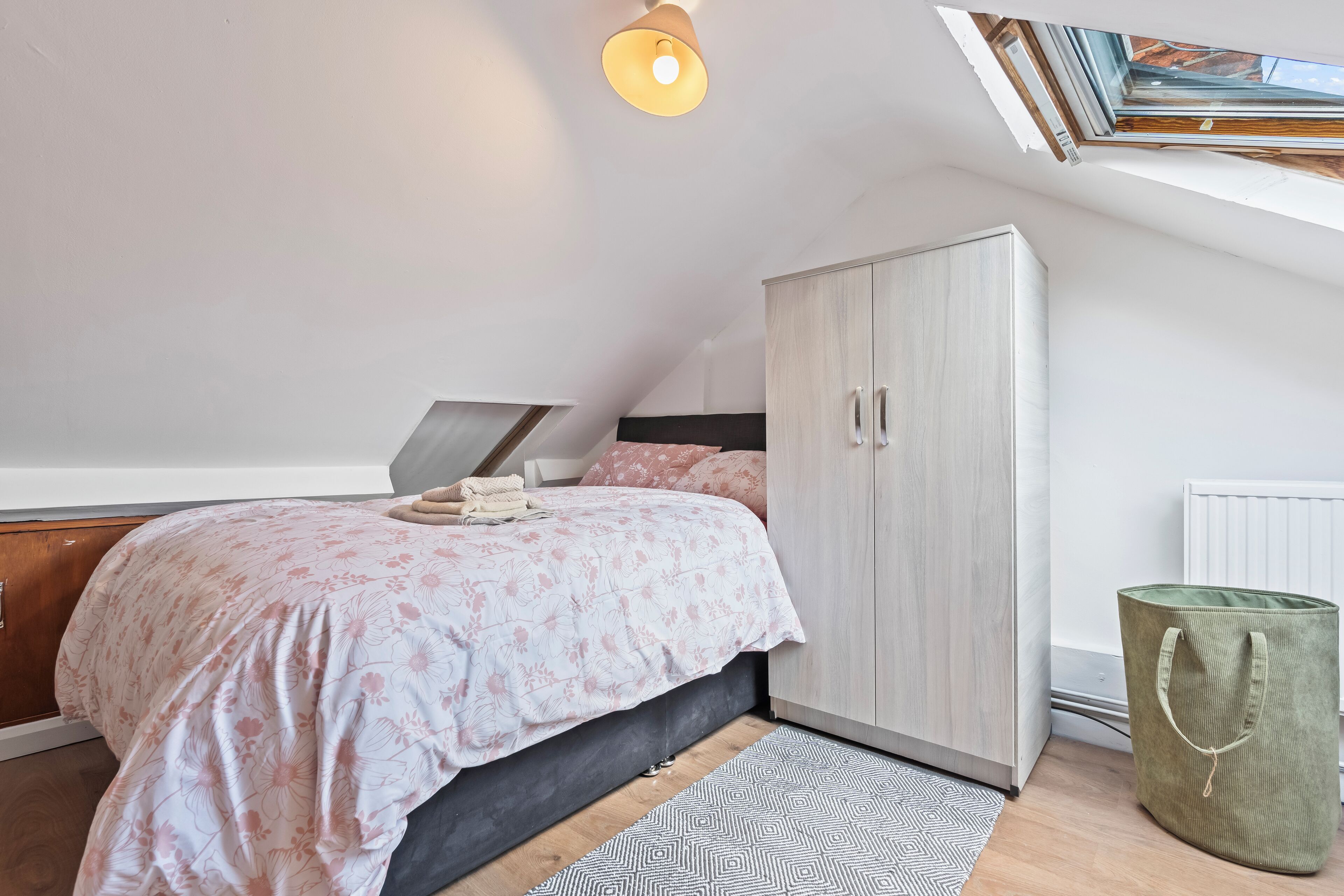 Een slaapkamer met een schuine plafond, een bed met bloemenbedrukking, een kledingkast en een dakvenster.