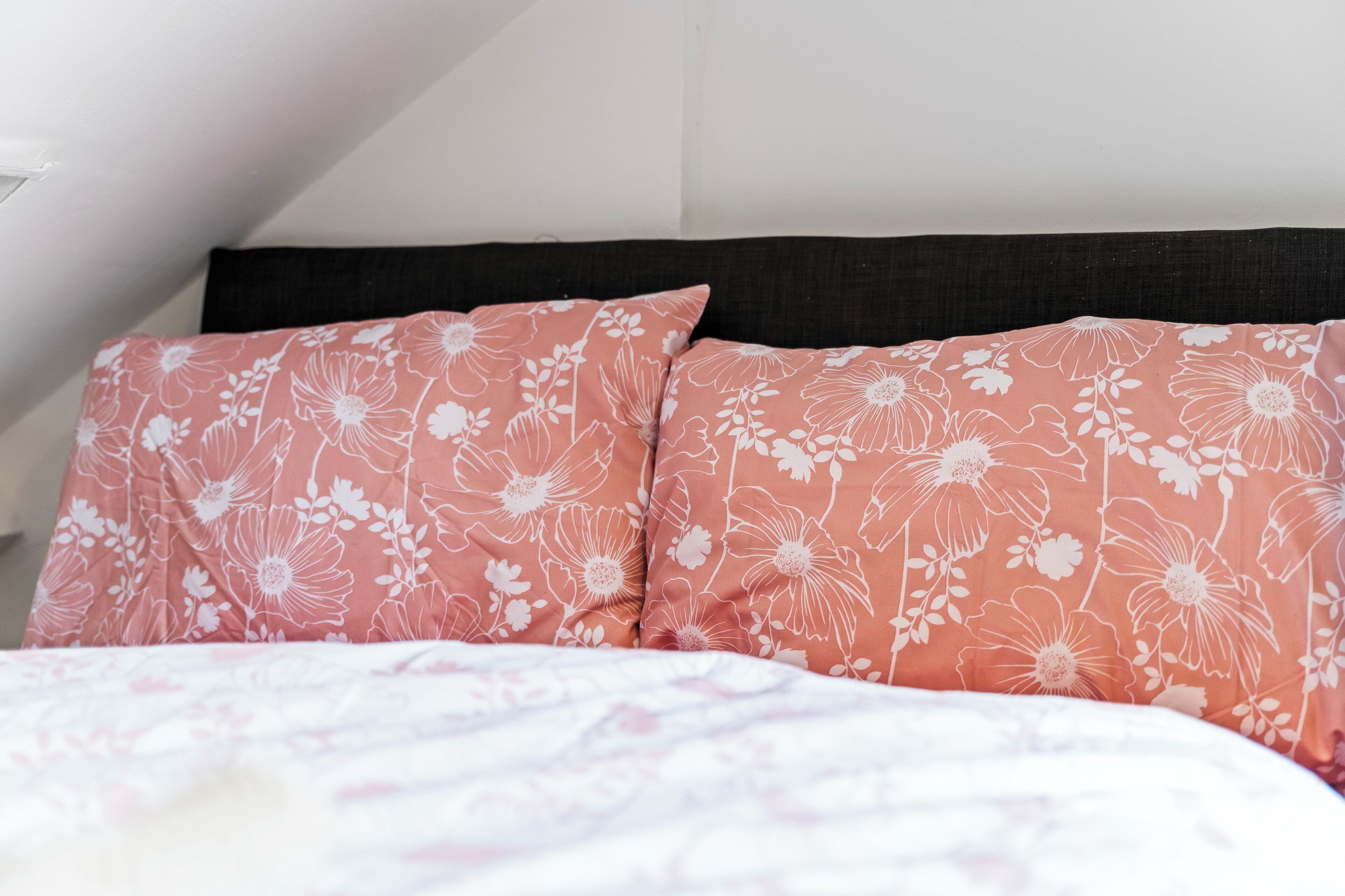 Ein Bett mit rosa blumigen Kissen und einer weißen blumigen Tagesdecke.