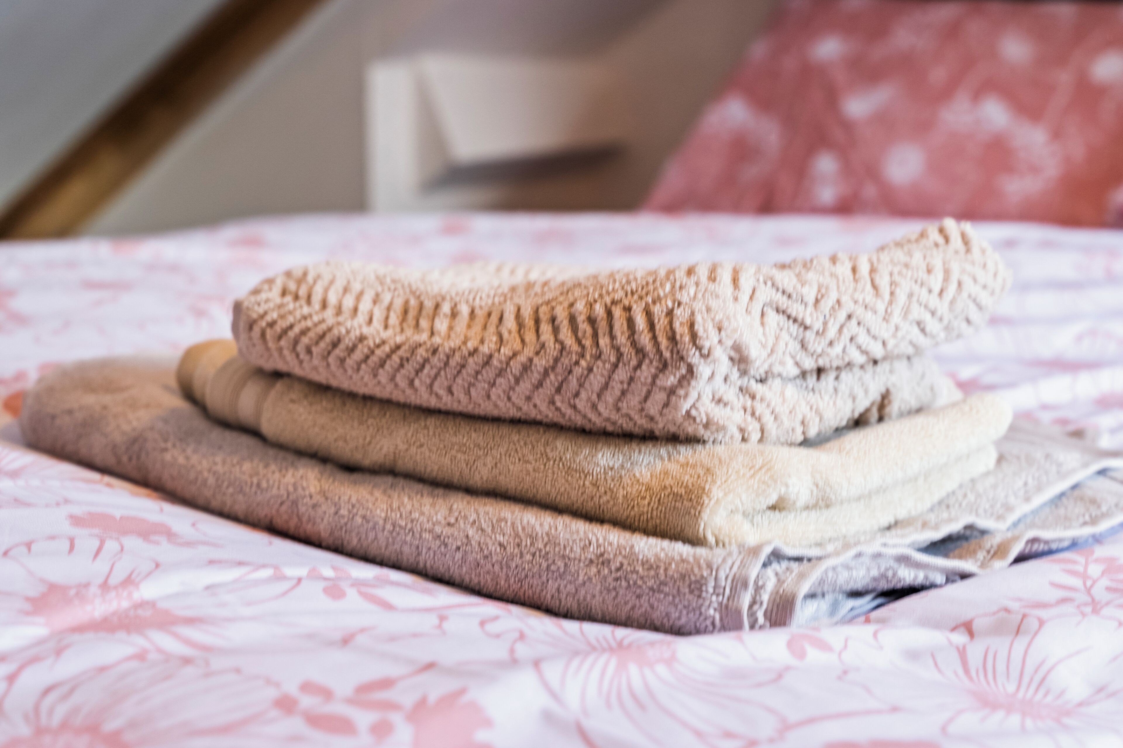 Uma cama com edredom estampado em flor e uma pilha de toalhas dobradas.