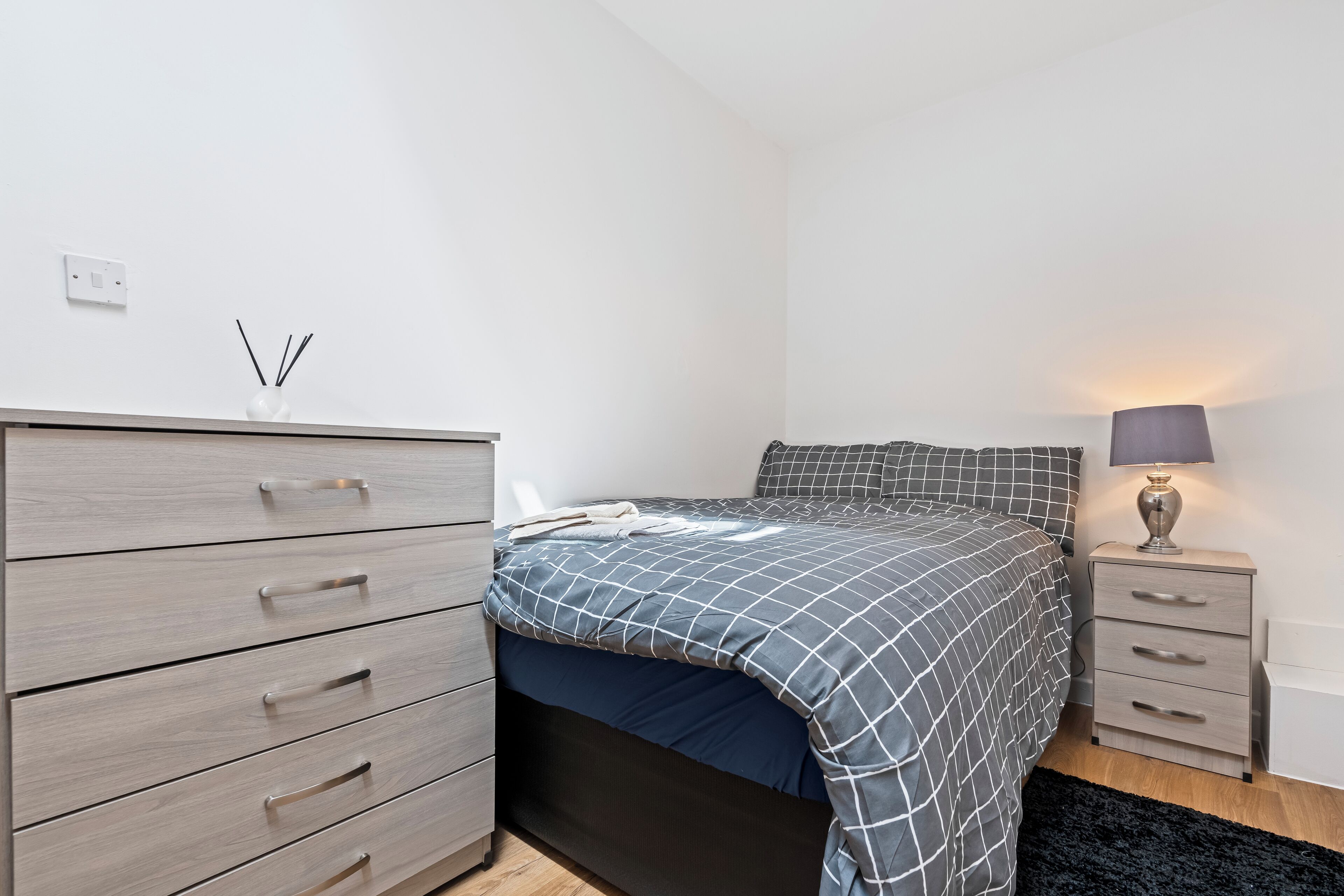 Een slaapkamer met een bed, een dressoir, een nachtkastje en een lamp.