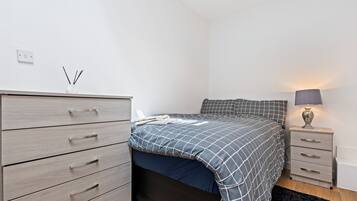 Een slaapkamer met een bed, een dressoir, een nachtkastje en een lamp.