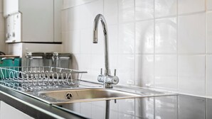 Una cucina moderna con lavello in acciaio inossidabile, scolapiatti e pareti rivestite di piastrelle bianche.