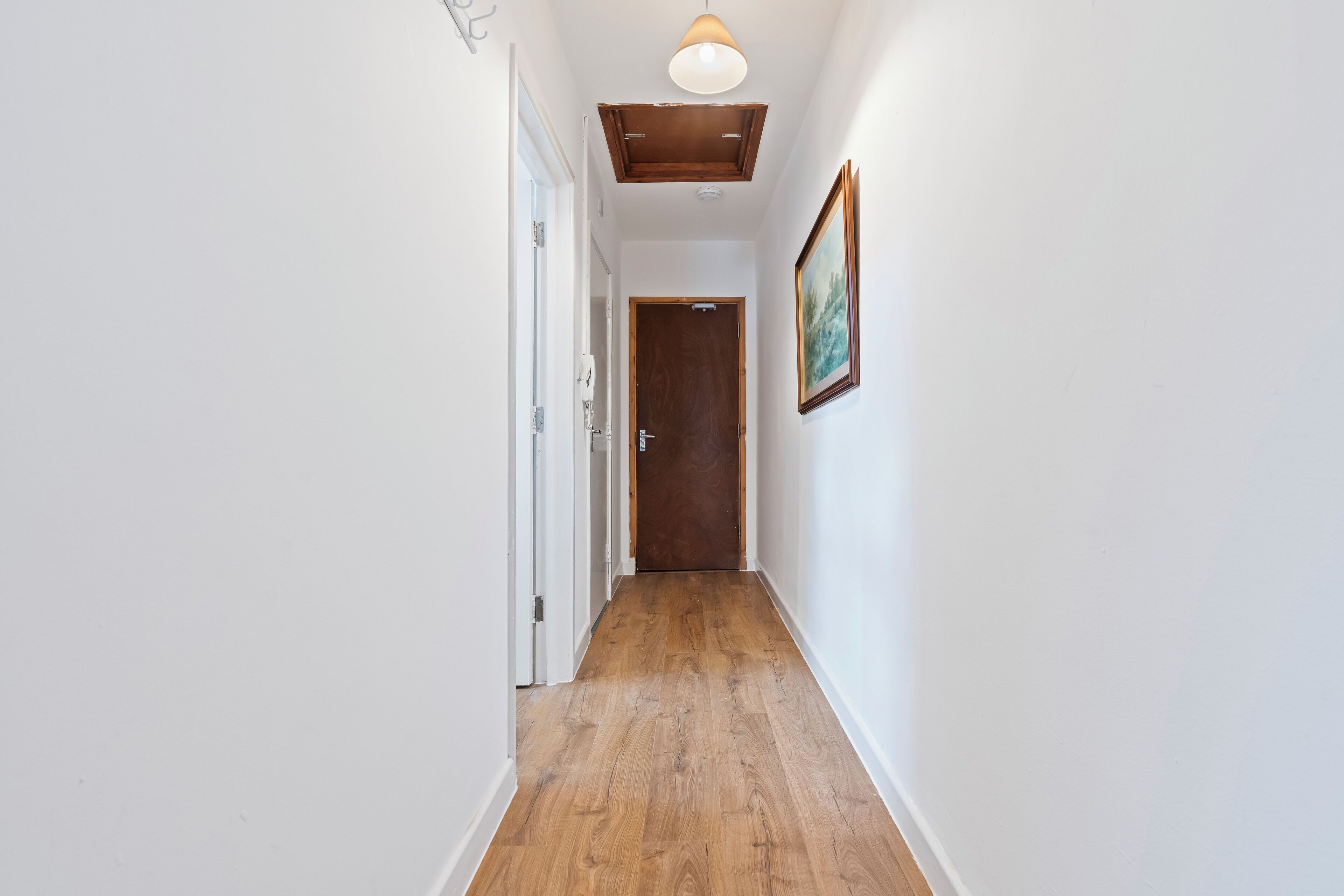 Un couloir étroit doté d’un plancher en bois, de murs blancs et d’un luminaire au plafond.