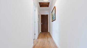 Un couloir étroit doté d’un plancher en bois, de murs blancs et d’un luminaire au plafond.