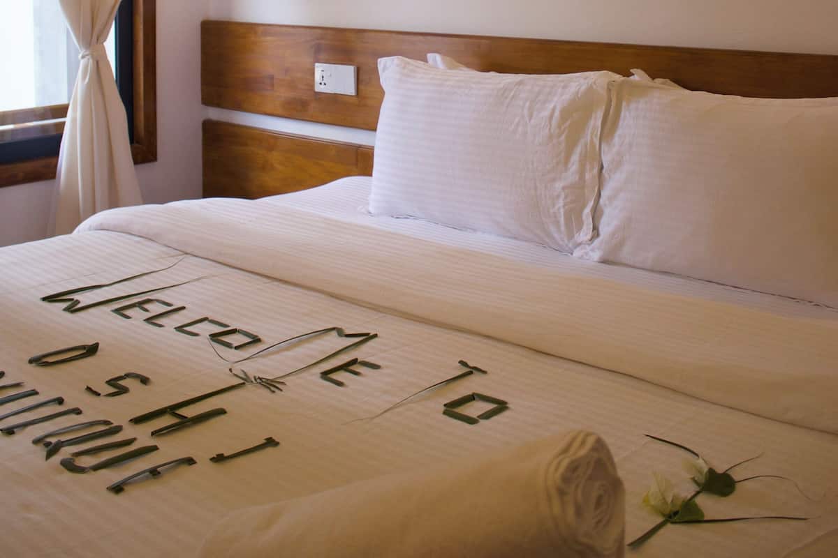A hotel room with a bed, a wall-mounted light, and three beach-themed paintings.