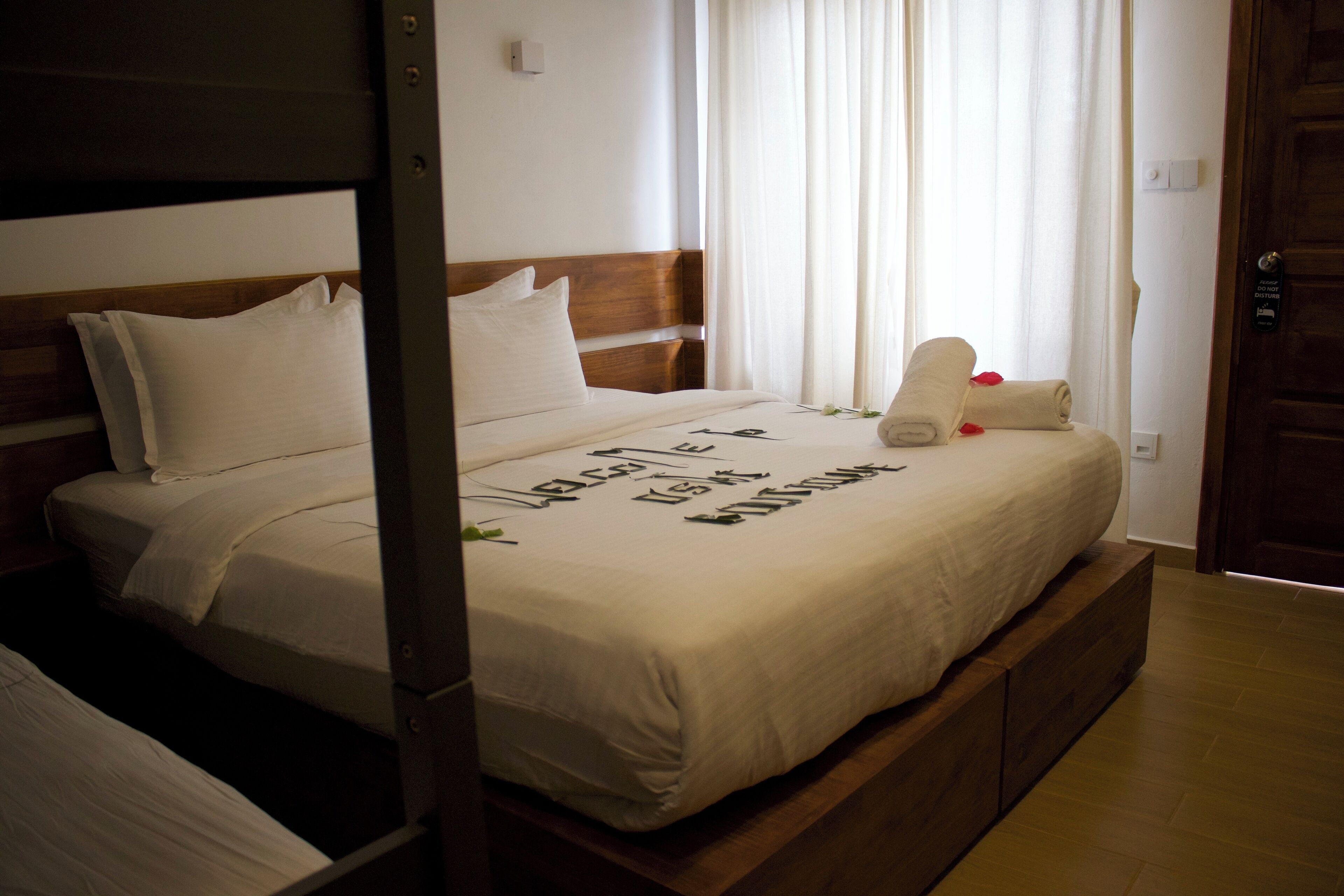 A neatly made bed with a wooden headboard, white linens, and a message written on the bedspread.