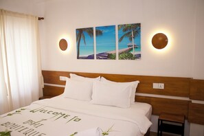 A hotel room with a bed, a headboard, a small table, and a wall-mounted picture of a beach scene. - Oshi Boutique  (Felidhoo)