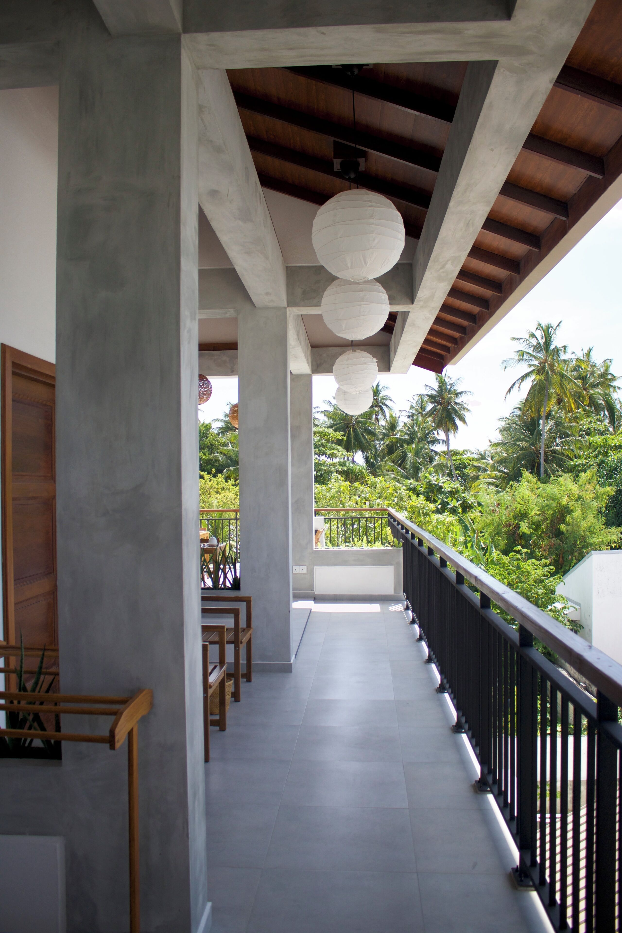 A covered balcony with a view of lush greenery and palm trees.