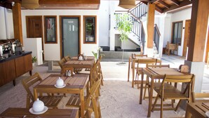 A spacious indoor area with multiple wooden tables and chairs, a staircase leading to an upper level, and a view of the outdoors. - Oshi Boutique  (Felidhoo)