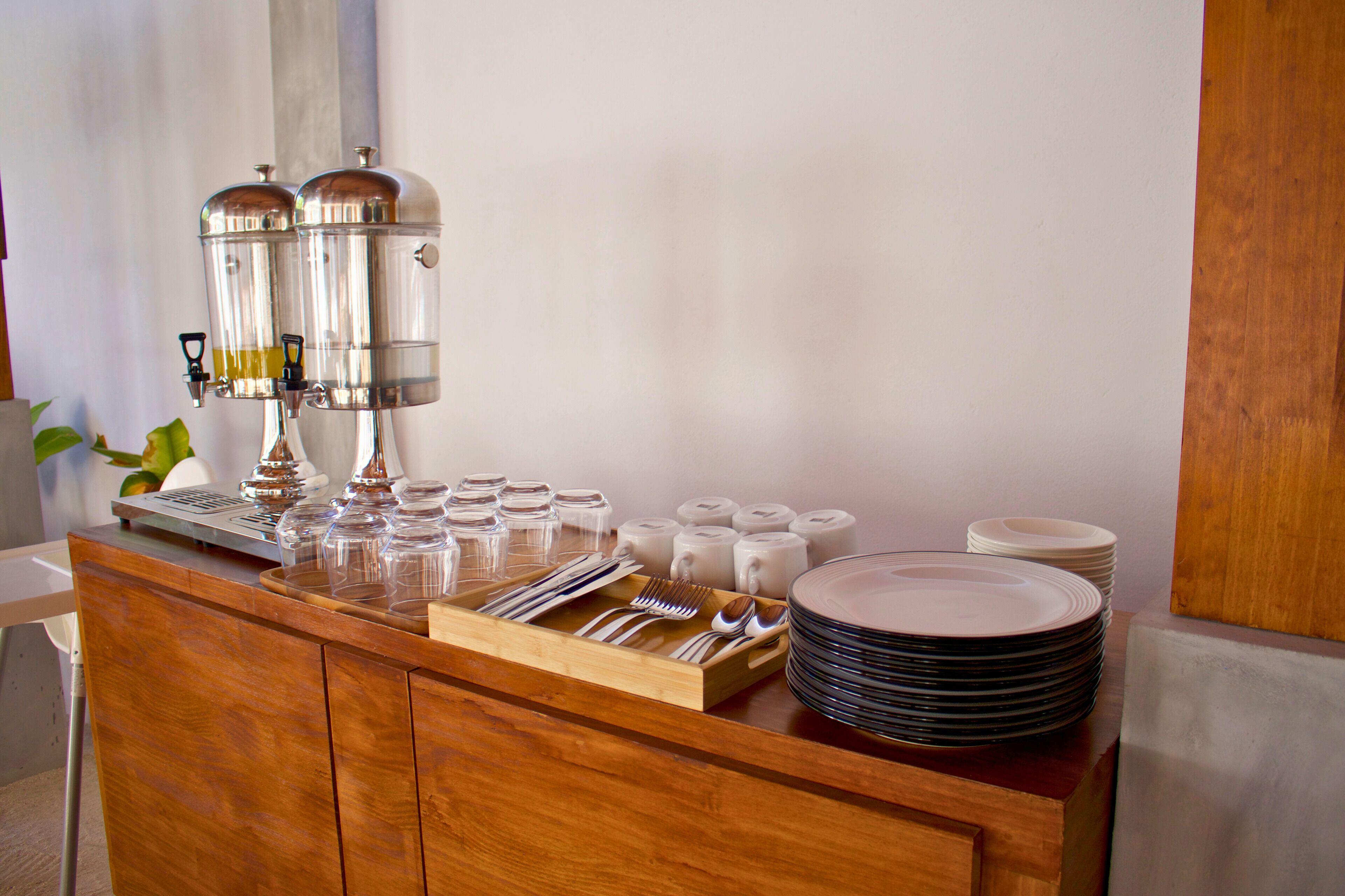 A buffet setup with a coffee machine, utensils, and stacked plates.
