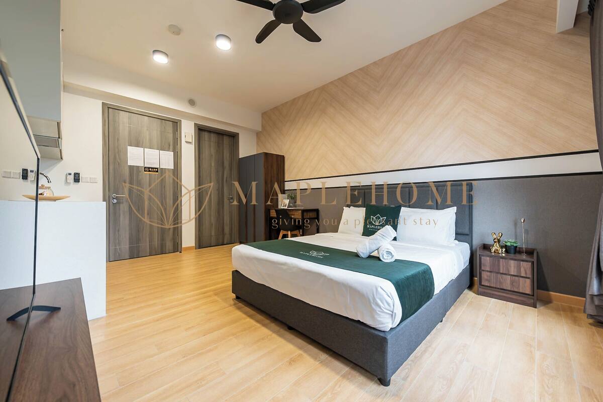 Een moderne hotelkamer met een groot bed, houten vloeren, een plafondventilator en een nachtkastje met een lamp.