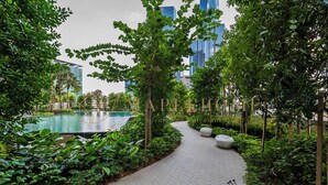 A landscaped pathway with a pool, surrounded by greenery and modern buildings in the background.
