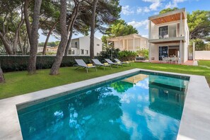 Ett modernt hus i två våningar med en swimmingpool, solstolar och en välskött gräsmatta.