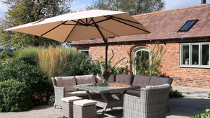 An outdoor patio with wicker furniture, a glass table, and a beige umbrella. - Relaxing Retreat in Shropshire (Eaton Constantine)