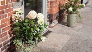 A brick building with a door and windows, potted plants with flowers, and a gravel ground. - Relaxing Retreat in Shropshire (Eaton Constantine)