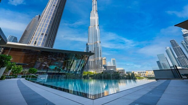 A modern building with a prominent tower, a reflective pool, and surrounding high-rise structures.
