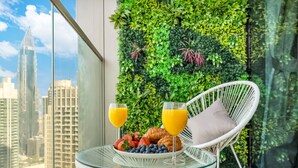 A balcony with a glass table, white wicker chair, breakfast with strawberries, blueberries, croissants, and orange juice glasses.