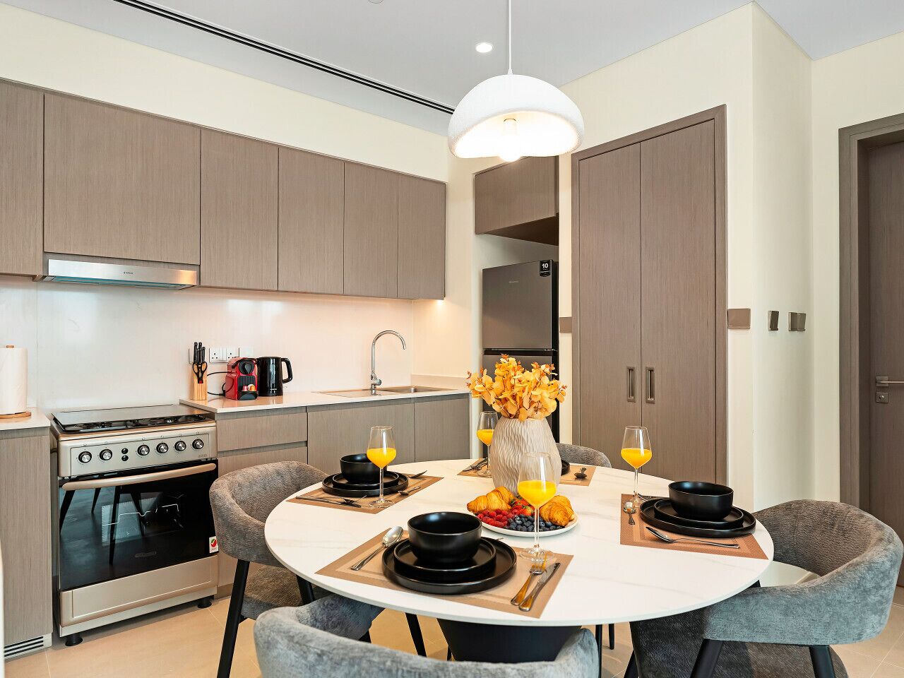 A modern kitchen with a dining area, featuring a round table, chairs, and a vase with flowers.