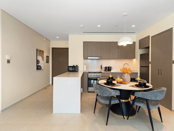 A modern kitchen with a central island, a dining area with a round table and chairs, and a hallway with artwork. - New 1BR | Burj Khalifa Infinity Pool | Dubai Mall (Dubai)