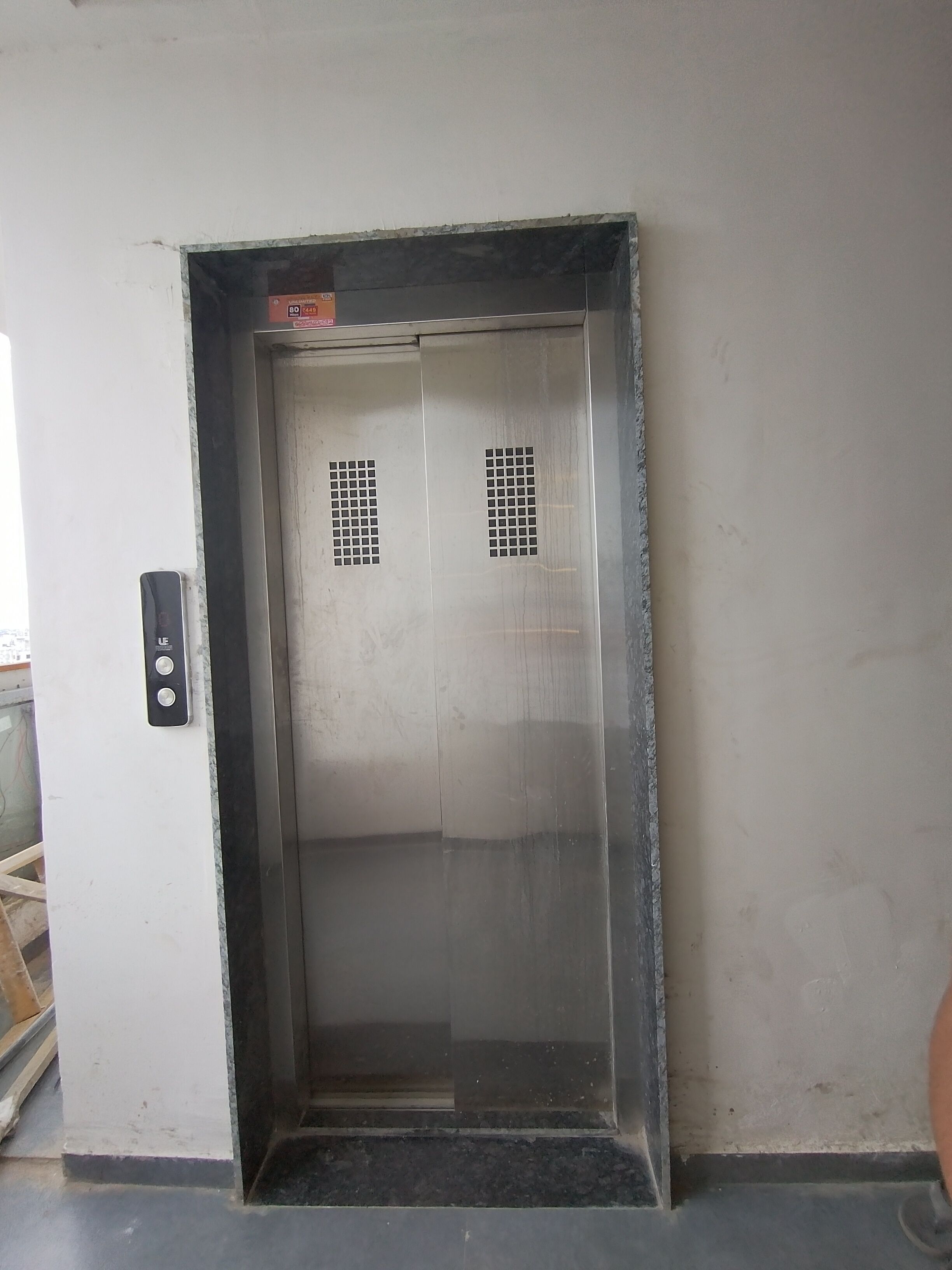 Puerta cerrada de un ascensor con un panel de control en la pared a la izquierda.