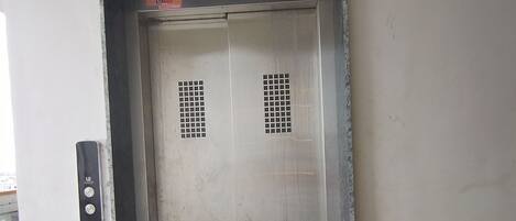 Puerta cerrada de un ascensor con un panel de control en la pared a la izquierda.