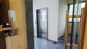 Un interior moderno con un vidrio que da a un pasillo, un elevador metálico y un suelo de mármol.