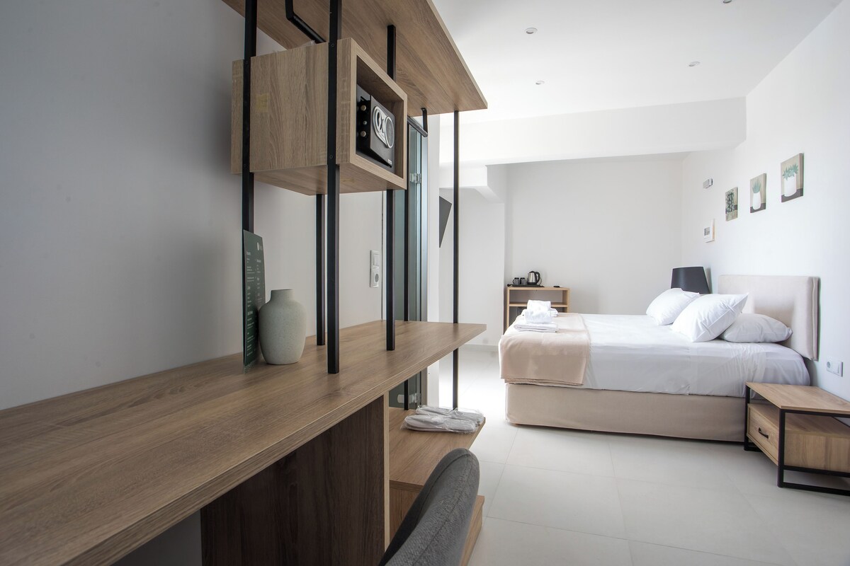 A modern bedroom with a wooden desk, a bed with white bedding, and a bedside table.
