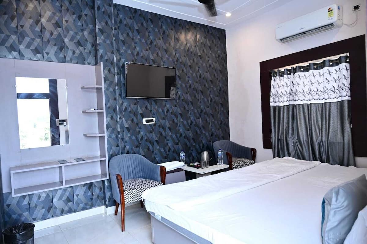 A hotel room with a bed, a desk with a chair, a TV, and a window with curtains.