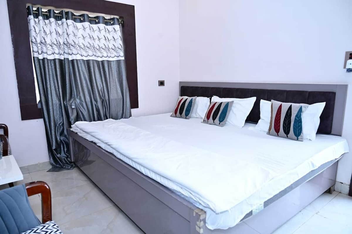 A bedroom with a bed, a chair, a window with curtains, and a bedside table.