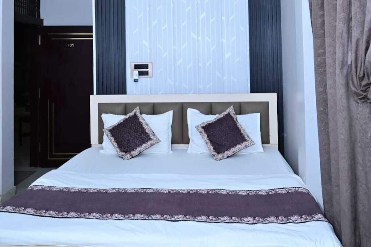 A hotel room with a bed, a ceiling fan, a window with curtains, and a door.