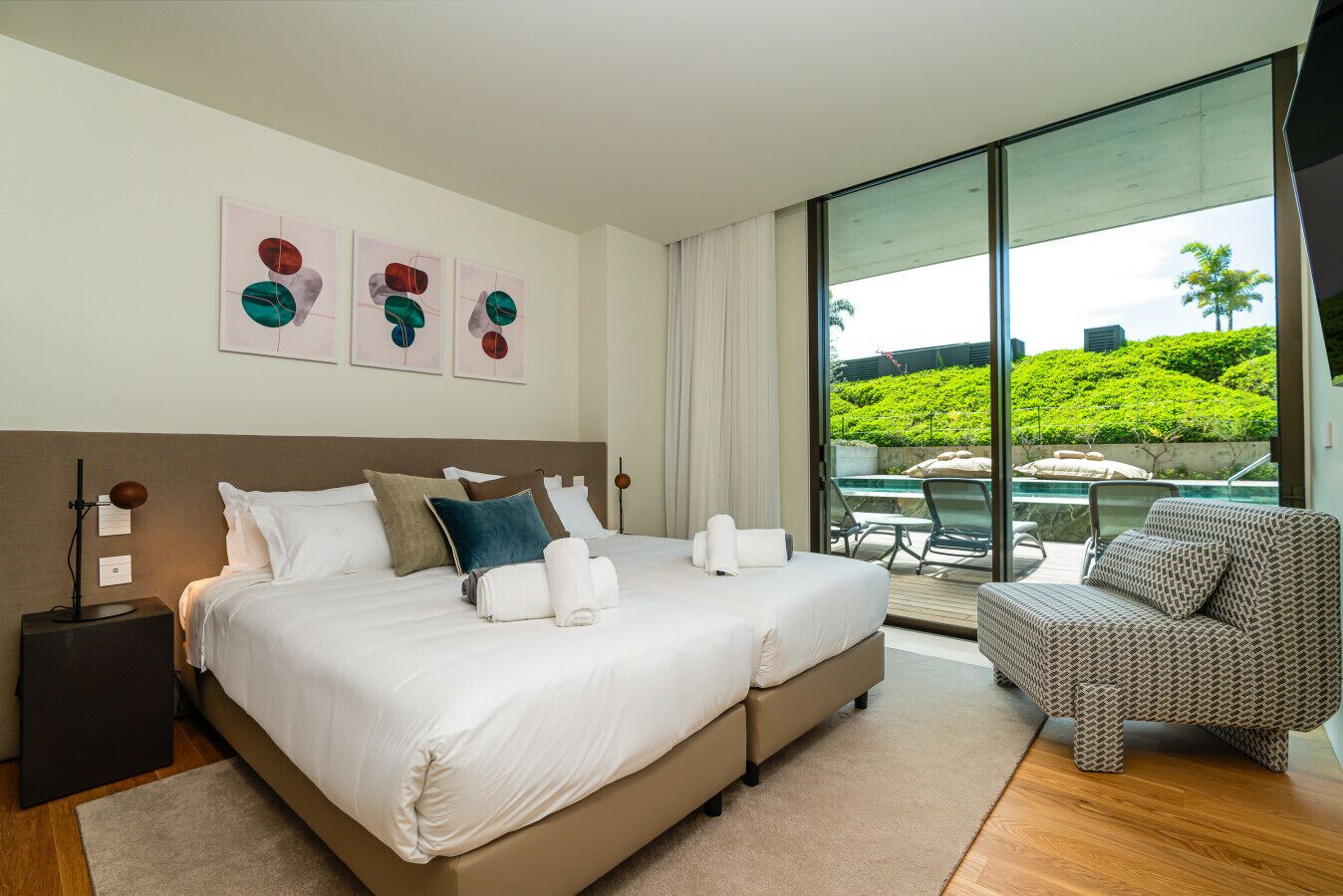 Una habitación de hotel moderna con una cama grande, un balcón con piscina y vistas a zonas verdes.