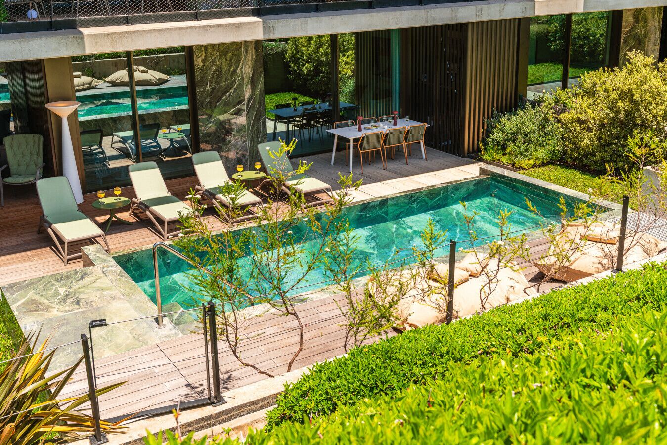 A modern outdoor pool area with lounge chairs, a dining table, and a view of the surrounding greenery.