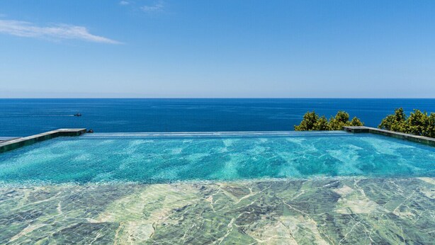 A clear view of a swimming pool with a view of the ocean and a small island with trees. - Private Heated Pool • Garden • Gym • Near the Sea (Funchal)