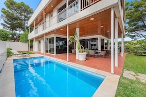 A modern two-story house with a swimming pool, outdoor seating, and a large window overlooking the pool.