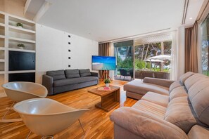 A modern living room with a sofa, chairs, a TV, and a balcony with outdoor furniture.