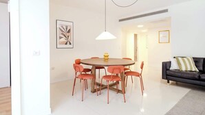 Een moderne eetruimte met een ronde tafel en oranje stoelen, een zwarte leren bank en een hanglamp.