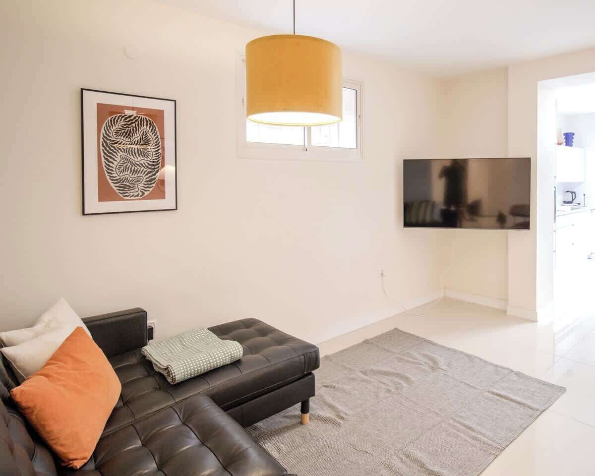 Un salon moderne avec un canapé en cuir noir, une grande fenêtre, un téléviseur à écran plat et une suspension jaune.