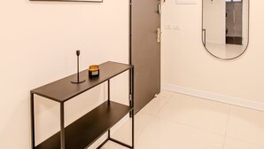 Een gang met een kunstwerk in een lijst, een gesloten deur, een bijzettafeltje met een kaars en een spiegel aan de muur.