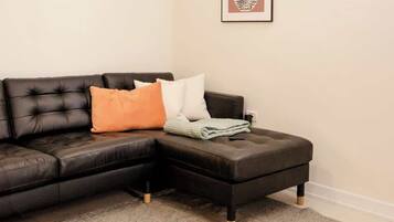 Een moderne woonkamer met een zwarte leren zithoekbank, een grijze vloerkleed, een houten salontafel, een hanglamp en een lijstwerk met een kunstwerk aan de muur.