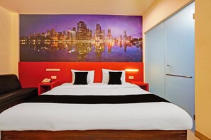 A hotel room with a large bed, a red headboard, a cityscape painting on the wall, and a blue door. - Townhouse Oak Malang near ITN Malang formerly Fariz Hotel Singosari (Malang)