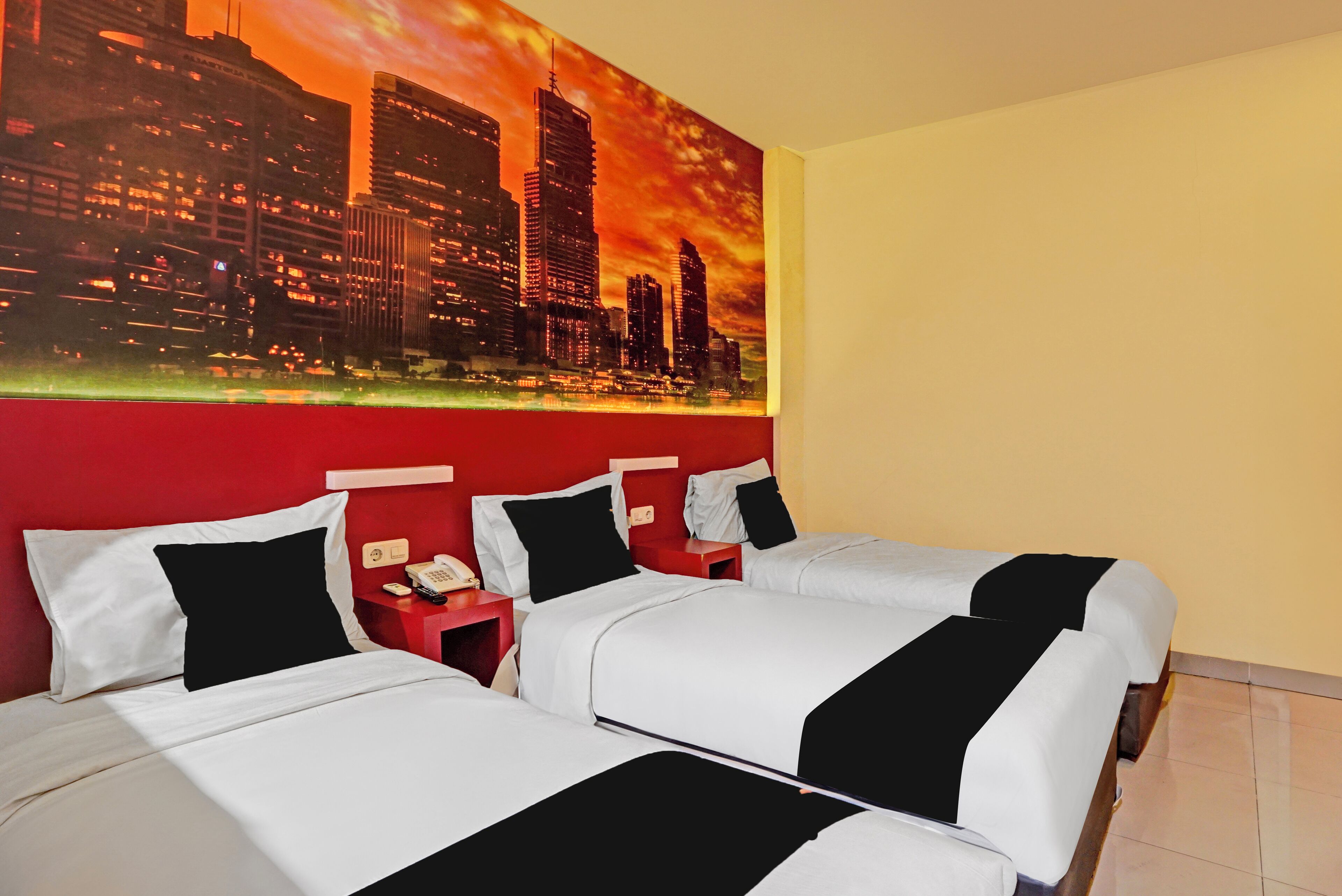 A hotel room with two beds, a red accent wall, and a cityscape painting.