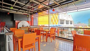 Un espacio exterior para comer con mobiliario de mimbre naranja y vistas a la ciudad.