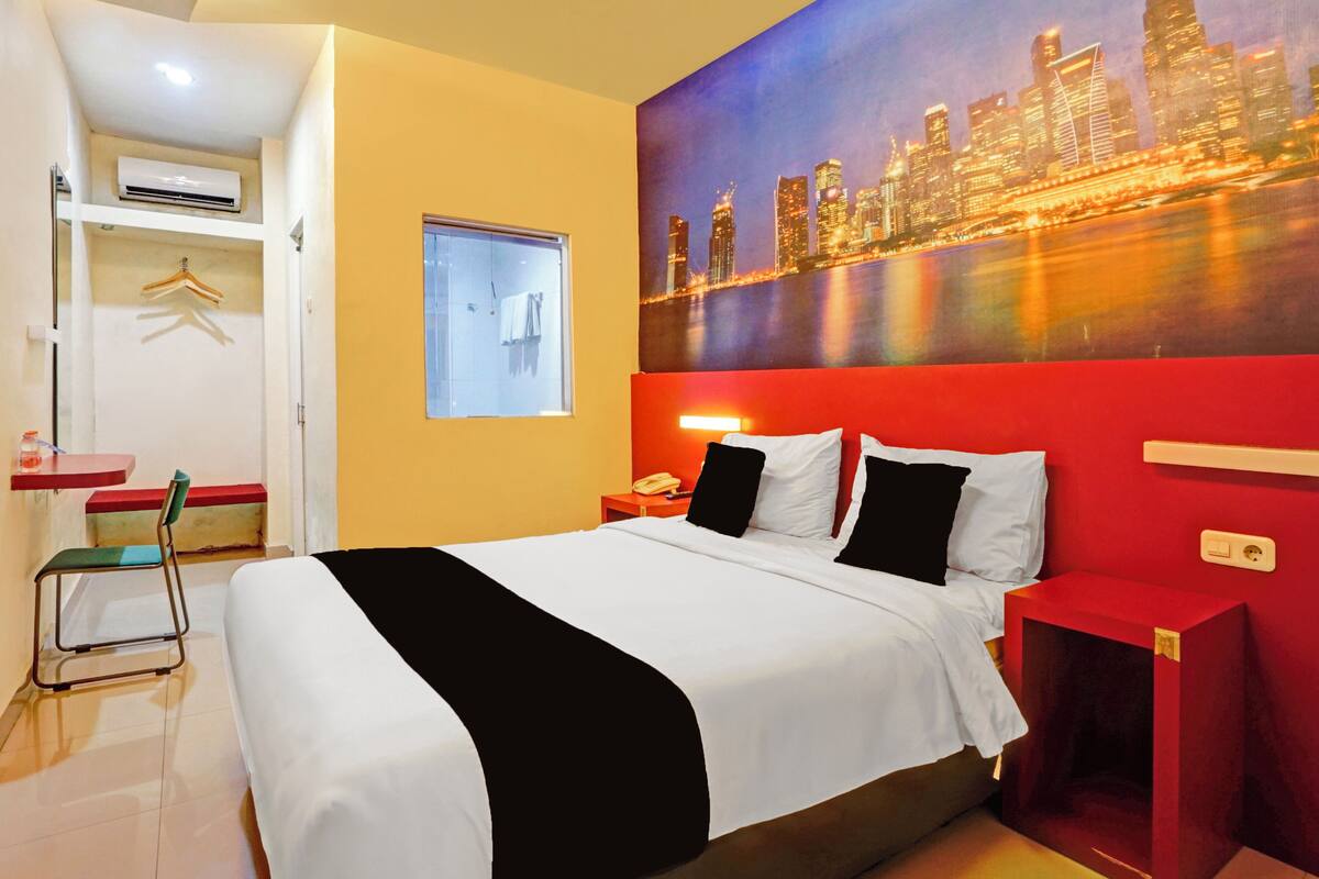 Ein Hotelzimmer mit Bett, Schreibtisch, Stuhl, Fenster und einem Stadtbild an der Wand.