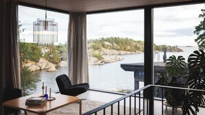 A modern room with a view of a river, a black chair, a wooden table, and large potted plants.