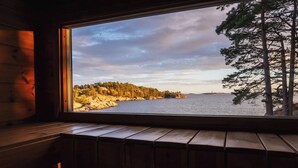 A wooden cabin interior with a large window overlooking a forested shoreline.